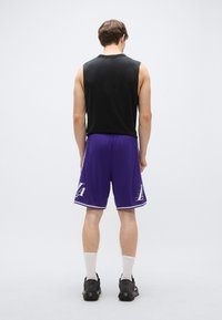 Maiou negru fără mâneci, asortat cu pantaloni scurți mov cu accente albe și un logo. Pantofi sport negri și șosete albe de gleznă.