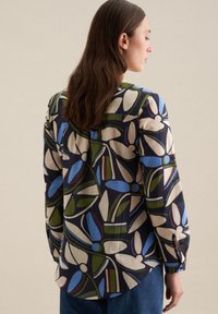 Camicia a fiore in blu navy, con motivi blu, verde e crema. Maniche lunghe con dettagli sui polsini, orlo curvo e tessuto testurizzato.