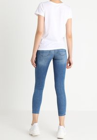 Bílé tričko s krátkým rukávem v kombinaci s modrými skinny džíny. Džíny mají vyšisovanou úpravu a čistý střih, doplněné bílými teniskami.