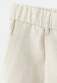 Lyse beige bomuldsbukser med detaljer som elastisk taljebånd, forlomme, bæltestrop og subtil tekstur i stoffet.