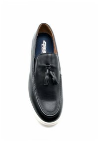 Chaussure noire en cuir à enfiler avec une finition lisse, bout arrondi et pampilles décoratives à l'avant. Semelle en caoutchouc blanche, design minimaliste.