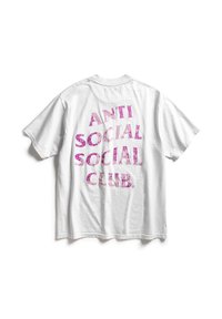 Biała bawełniana koszulka z odważnym, błyszczącym różowym napisem na plecach, który brzmi "ANTI SOCIAL SOCIAL CLUB." Okrągły dekolt, krótkie rękawy.