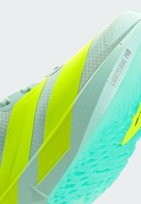 Scarpa da calcio con un corpo verde menta, strisce diagonali gialle, superficie testurizzata e una suola azzurro chiaro etichettata "LIGHTSTRIKE PRO."
