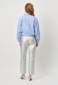 Gestreepte blauwe shirt met een relaxte pasvorm, gecombineerd met glanzende zilveren wijde broek, met een gladde textuur en zichtbare achterzakken.