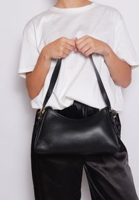 Borsa a mano in pelle nera con forma curvata, caratterizzata da una texture Liscia e una lunga tracolla. Dettagli in metallo dorato vicino ai punti di attacco.