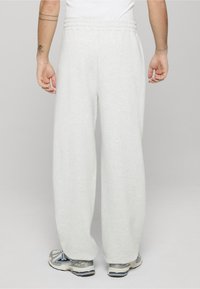 Jasnoszare spodnie dresowe wykonane z miękkiego materiału, z elastycznym paskiem w talii i luźnym krojem, w połączeniu z butami sportowymi.