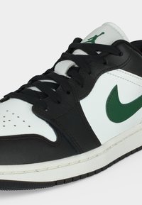 Μαύρο και άσπρο αθλητικό παπούτσι Nike με πράσινο λογότυπο Swoosh, μαύρα κορδόνια και πράσινο λογότυπο Jumpman στην άσπρη γλώσσα του παπουτσιού.
