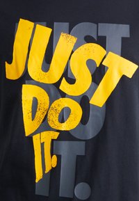 Camiseta preta com um design de texto em amarelo e cinza em destaque. O texto diz "FAÇA ACONTECER" com uma textura desgastada.