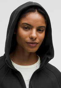 Czarna bluza z kapturem na zamek, z podszewką w kapturze, posiadająca subtelne detale w szyciu oraz kieszeń typu kangur. Nosi się ją na białej koszulce.