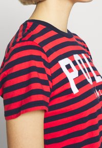 Röd och marinrandig t-shirt i bomull, med rund halsringning och en djärv "POL"-tryck i vitt fram. Korta ärmar.