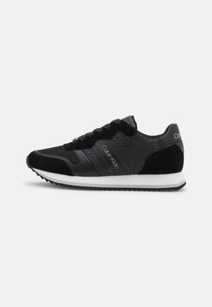 Baskets noires Calvin Klein avec motif de logo en relief, semelle intermédiaire blanche et semelle extérieure noire, vues de côté sur fond blanc.