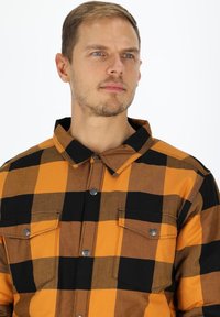 Flannel skjorte med sort og orange ternet mønster, har spidse kraver, to brystlommer og sølvfarvede trykknapper.
