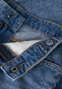 Jeans iz denima v modri barvi, z vidnimi šivi in gumbnim zapiranjem. Odkrita bela podloga z detajlom z zadrgo.