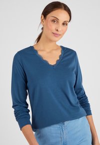 Blauwe lange mouwen T-shirt met een V-hals en kantdetails. Gemaakt van zachte stof, heeft een relaxte pasvorm en een gladde textuur.