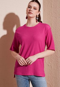 Fuchsia short-sleeve top made of textured fabric featuring a crew neckline and side slits, paired with light-wash denim jeans.