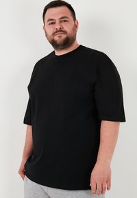 Černé bavlněné tričko s krátkým rukávem, kulatým výstřihem a volným střihem. Hladká textura, bez viditelných vzorů nebo akcentů. Ležérní design.