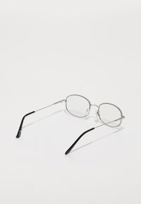 Lunettes en métal avec des verres ovales transparents, des branches argentées et des embouts noirs. Design minimaliste sans logos ni motifs visibles.