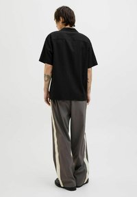 Camisa negra de manga corta con un patrón texturizado, combinada con pantalones anchos grises que tienen franjas laterales crema y calzado negro.