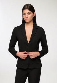 Blazer nero con scollatura a V profonda, chiusura a un bottone, vestibilità aderente e spalle strutturate. Presenta due tasche anteriori e un tessuto morbido.