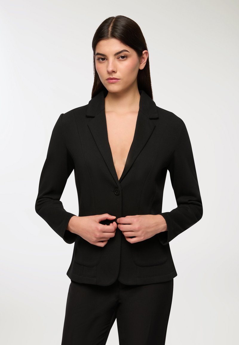 Blazer nero con scollatura a V profonda, chiusura a un bottone, vestibilità aderente e spalle strutturate. Presenta due tasche anteriori e un tessuto morbido.