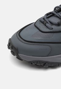 Grau Wanderschuh mit synthetischem Obermaterial, Netzeinsätzen, strukturiertem Gummisecond und auffälligem Schnürsystem; mit Logo an der Seite.