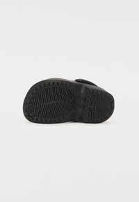 Calzado negro con una suela de goma texturizada, que presenta un patrón de relieve para mayor agarre. El zapato tiene un perfil plano y un diseño simple y minimalista.