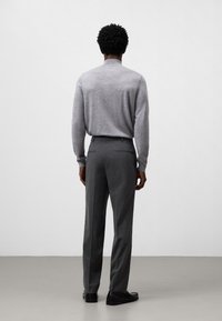 Maglione grigio in lana con colletto alto, abbinato a pantaloni grigi su misura. L'outfit presenta un design a gamba dritta e scarpe nere.