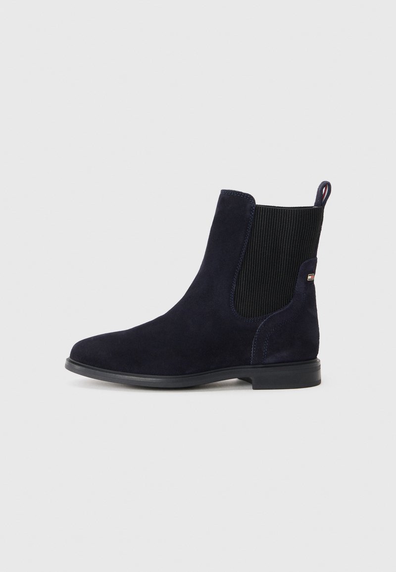 Bota Chelsea de ante azul marino con panel lateral elástico negro, tacón bajo y lengüeta en la parte trasera sobre un fondo claro.