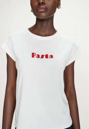 Femme portant un T-shirt blanc avec le texte rouge « Pasta » centré sur la poitrine, manches courtes retroussées et boucles d'oreilles créoles en or.