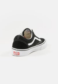 Zapatilla de ante negro con un diseño de olas blancas, suela de goma blanca y un logo rojo de Vans en el talón. Punta redondeada, cuello acolchado y estilo minimalista.