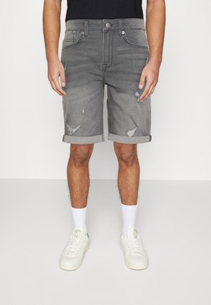 Szare dżinsowe szorty z podwiniętymi mankietami, zniszczonymi detalami i klasycznym pięciopocketowym krojem, połączone z białymi trampkami i skarpetami.