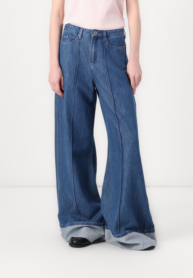 Bredde ben denimjeans med en mørkeblå vask. Har høy midje, kontrasterende sømmer og brettede mansjetter som avslører en lysere denim.