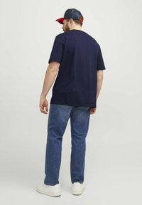 Navy blue cotton t-shirt with a relaxed fit, paired with light blue denim jeans. Features a white sole sneaker and a cap with red accents.
