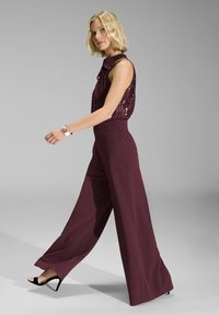 Pantaloni larghi bordeaux in tessuto morbido abbinati a un top senza maniche di paillettes dello stesso colore. Accenti di semplici tacchi neri visibili.