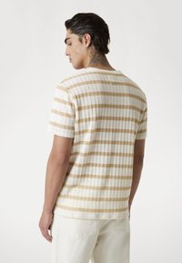 Korte mouwen shirt met beige en witte horizontale strepen. Gebreide textuur met een losse pasvorm. Ronde halslijn en lichtjes verlaagde schouders.
