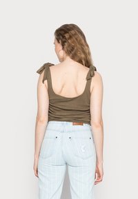 Top de alças com riscas em verde-azeitona; combinado com jeans de cintura alta, listrados em azul claro, com bolsos traseiros e detalhe de logotipo.