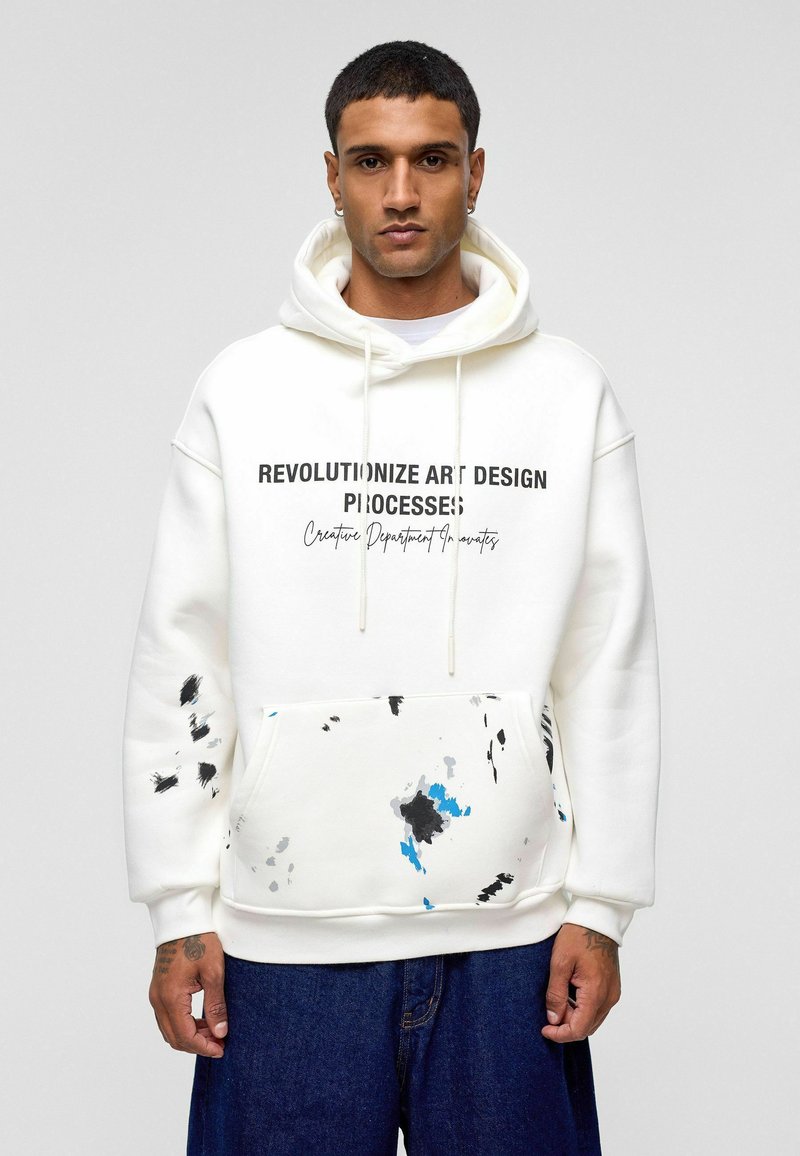 Witte hoodie met zwarte opdruk, voorzak en kleurrijke verfspatten in blauw, grijs en zwart. Zacht katoen materiaal.