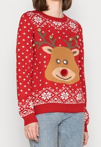 Pull rouge en tricot avec un motif de visage de renne, des flocons de neige blancs, des accents dorés et une finition texturée.