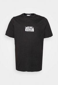 Svart bomulls t-shirt med en rektangulär vit grafisk design med texten "Calvin Klein" i ett modernt typsnitt. Kortärmad och med rund halsringning.