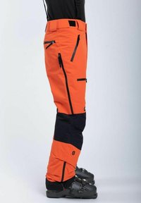 Kirjava oranssit lasketteluhousut mustilla yksityiskohdilla, joissa on useita vetoketjullisia taskuja ja klipsuja, valmistettu kestävästä säänkestävästä materiaalista.