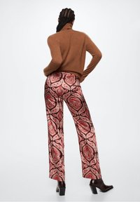Pull en tricot marron, pantalon large à motifs avec un design paisley rouge et beige, complété par des bottines à talons noires.