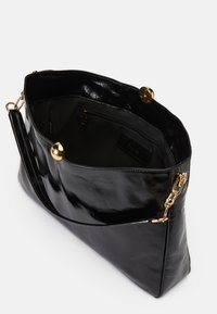 Bolso de mano de charol negro con una textura suave, herrajes en tono dorado, bolsillo interior con cremallera y una correa para el hombro.