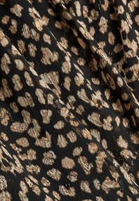 Tessuto nero con un motivo a stampa leopardata in beige e accenti dorati. La texture appare leggera e leggermente trasparente con una leggera lucentezza.