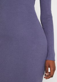 Abito viola a coste con maniche lunghe, design aderente e finitura texture. Il tessuto è elastico e liscio, mettendo in risalto le curve del corpo.