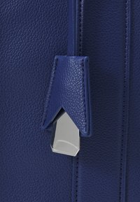 Gros plan sur un sac en cuir bleu grainé avec un rabat en cuir triangulaire et une boucle métallique argentée.