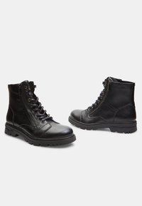 Botine din piele neagră până la gleznă, cu vârf rotund, șireturi în față, fermoar pe lateral, talpă din cauciuc cu model și detalii de cusătură întărită.