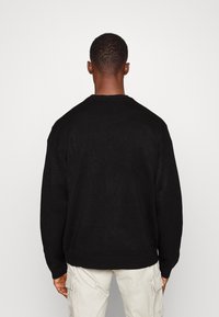 Suéter de punto negro de gran tamaño con cuello redondo, puños y dobladillo acanalados, con una tela suave y texturizada. Vista trasera mostrada.