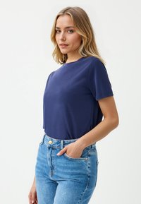 Marineblauw T-shirt met korte mouwen, ronde halslijn, zachte stof, losse pasvorm, gecombineerd met high-waisted lichtblauwe denim jeans.