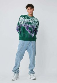Pull vert en maille avec un dégradé violet et blanc, col rond. Associé à un jean ample bleu clair et des baskets blanches.