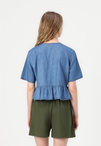 Modra denim majica s kratkimi rokavi in peplum robom, z okroglo ovratnikom. V kombinaciji z zelenimi kratkimi hlačami. Teksturni material.